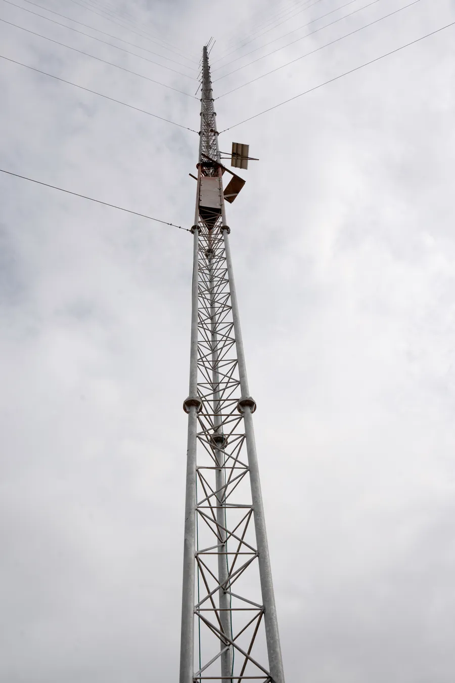 Looking up the top section of a met mast at its sensor booms and antenna against cloud