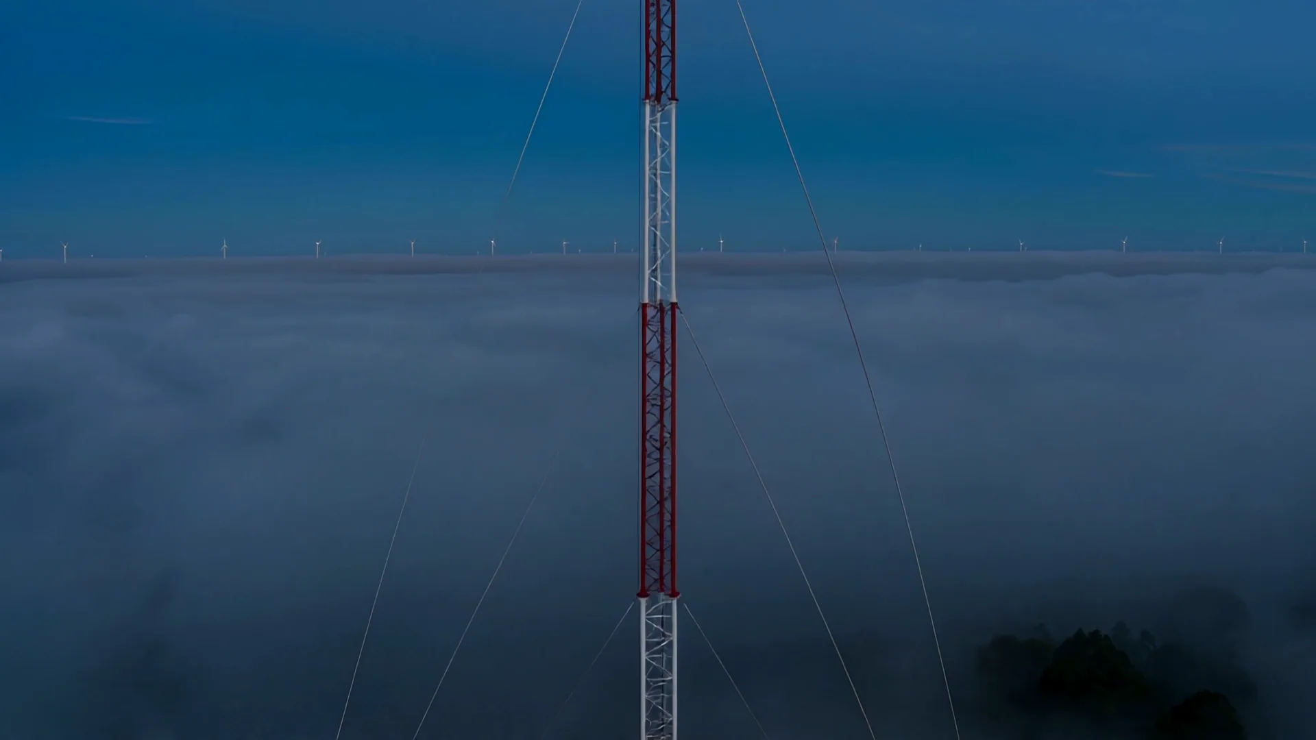 Mid-structure of the mast: galvanised lattice and pre-tensioned guy wires in fog