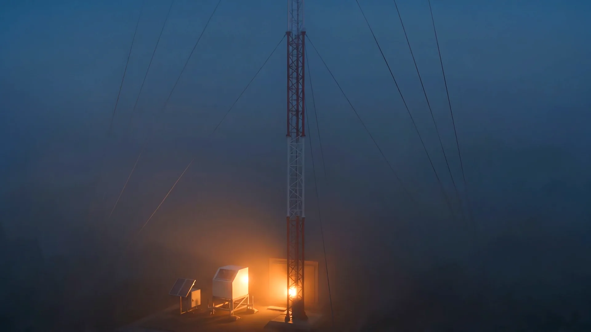 The warm-lit base of the mast at ground level in the fog